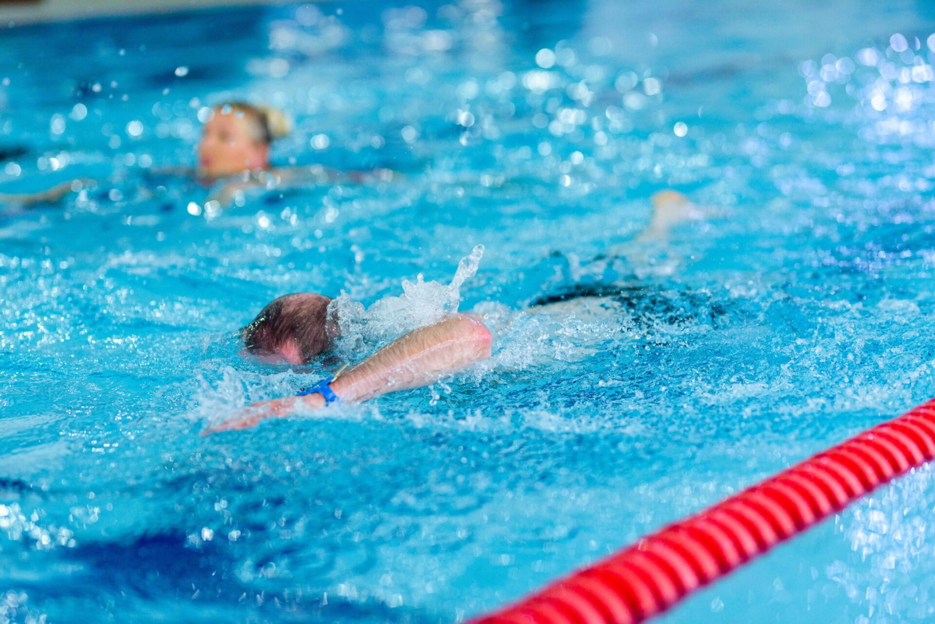 A child and adult swim together in a pool, with the child mid-splash.