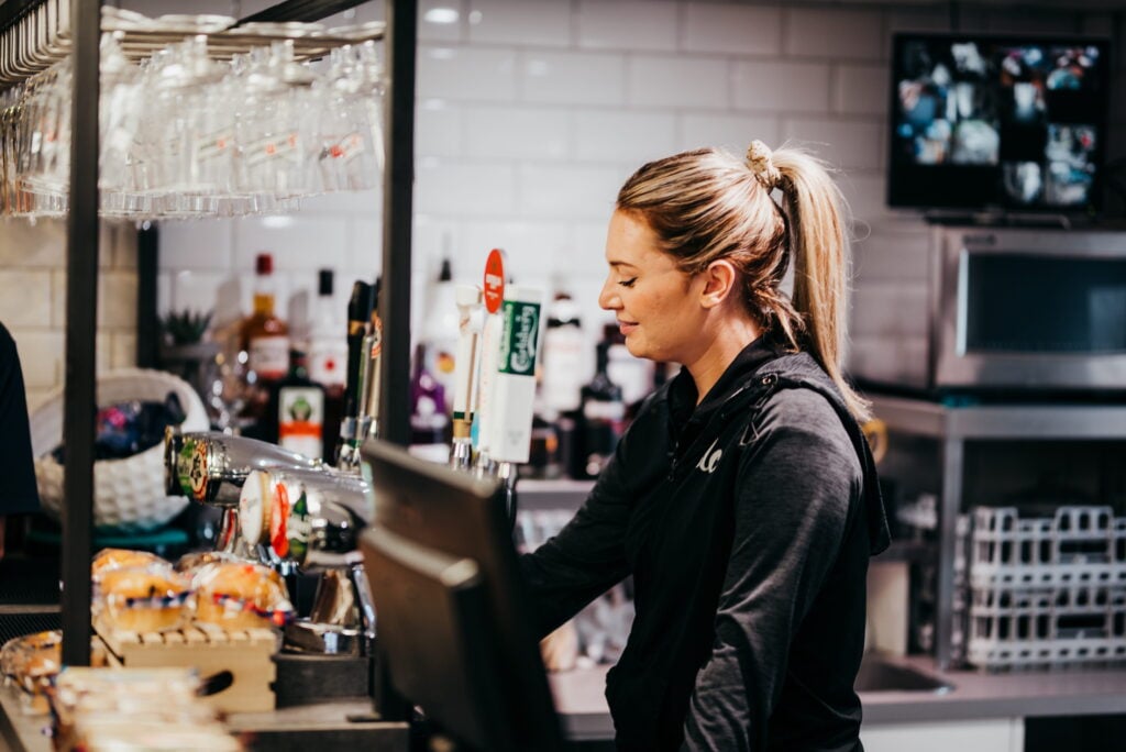 A bartender pours a drink behind the bar in a restaurant setting.