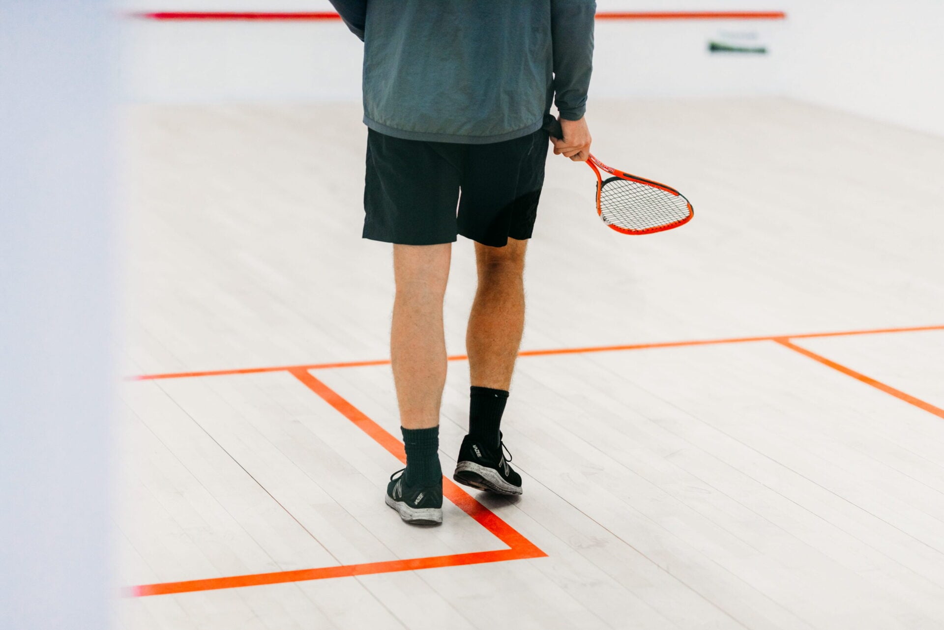 A close-up of a squash player's legs and racket on an indoor squash court."