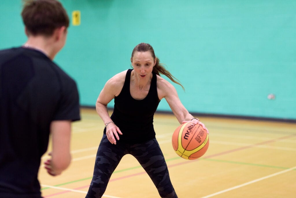 A woman dribbles a basketball on an indoor court while another player looks on