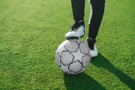 A close-up of a soccer ball resting near a player's feet on a grass pitch.