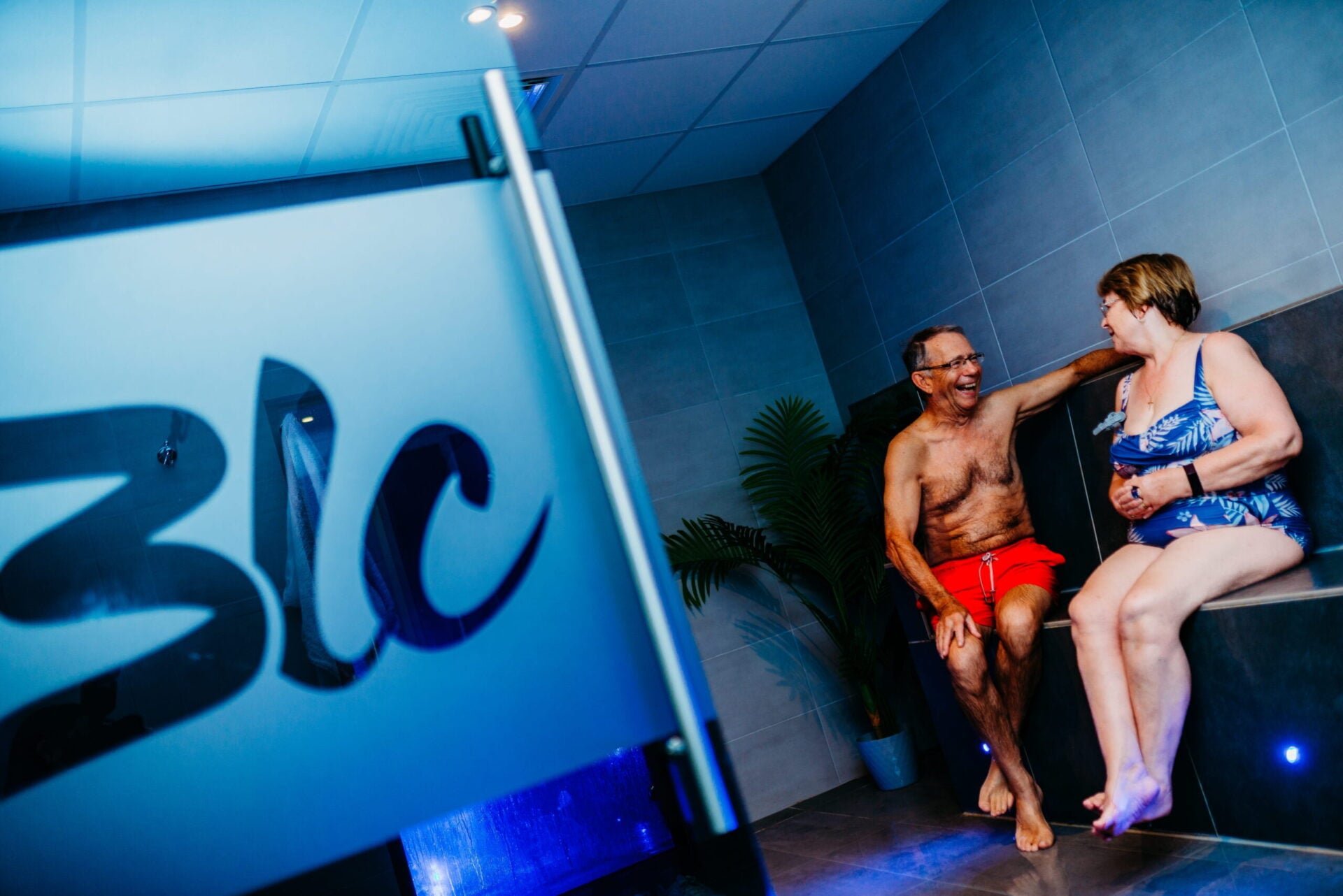 Two men chat and smile together in a changing area near a BLC-branded wall.