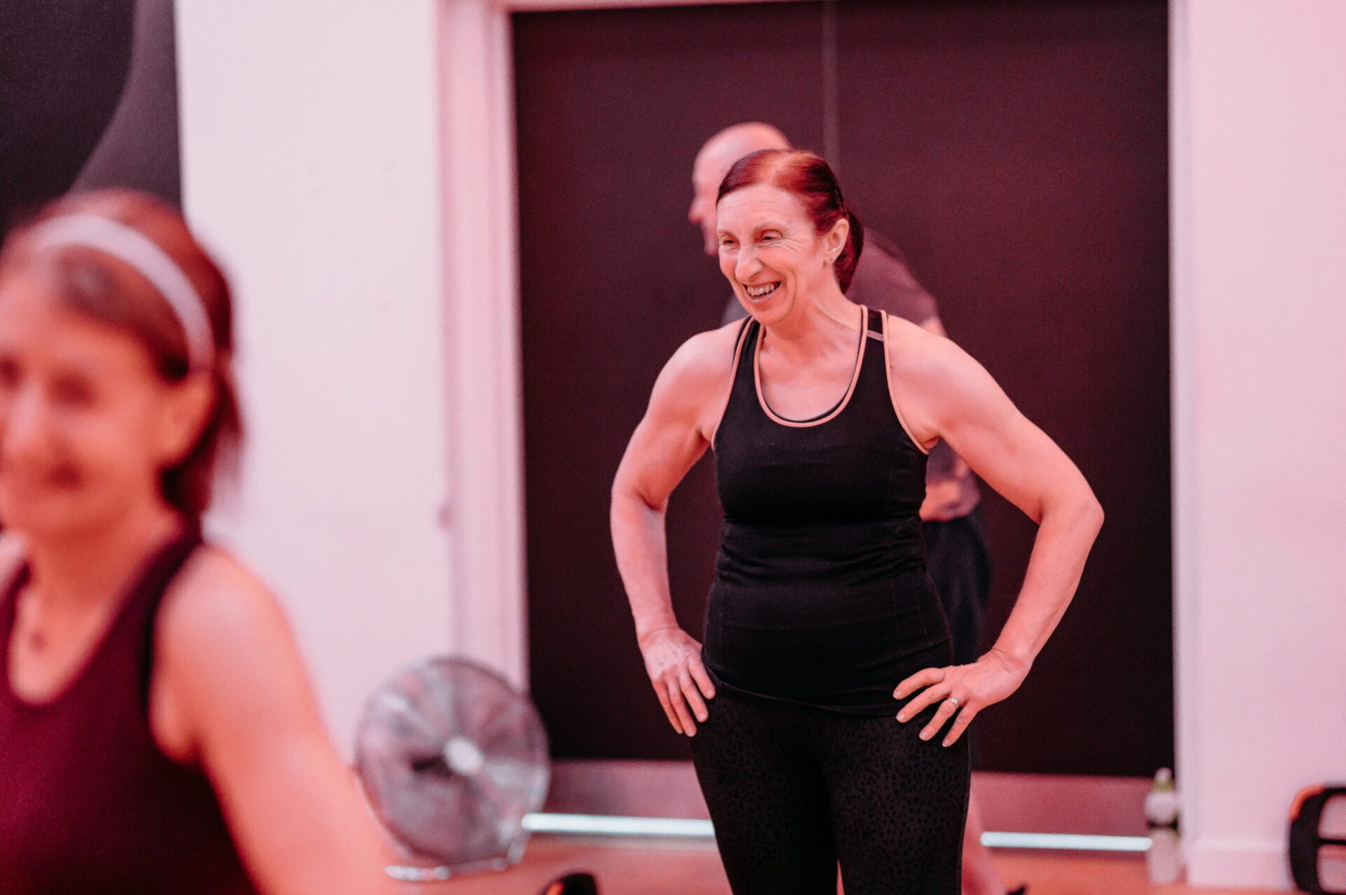 A woman rests her hands on her hips while wearing gym attire in a fitness studio.