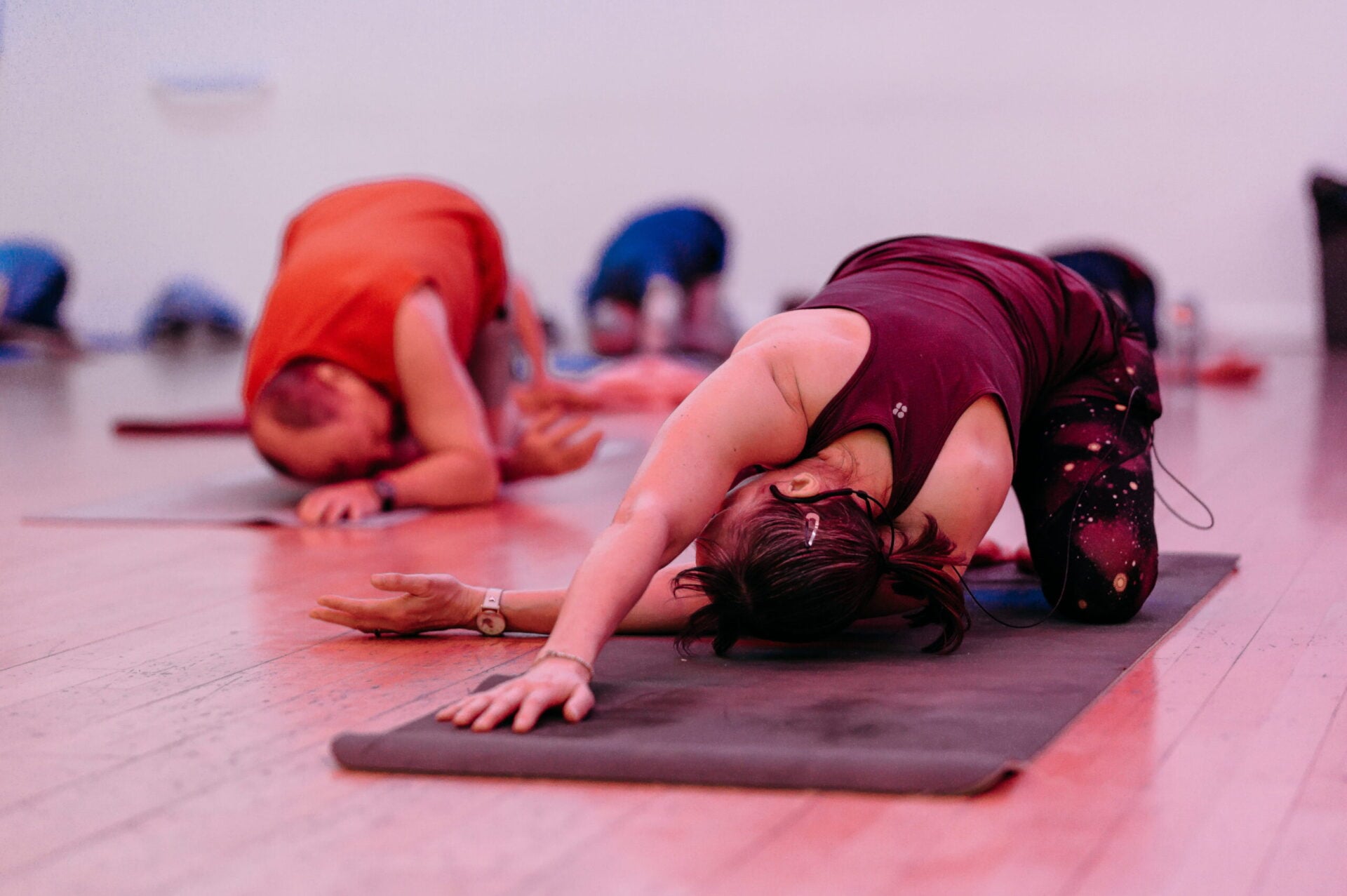 A group fitness class practises yoga stretches, with participants spaced across mats on the floor.