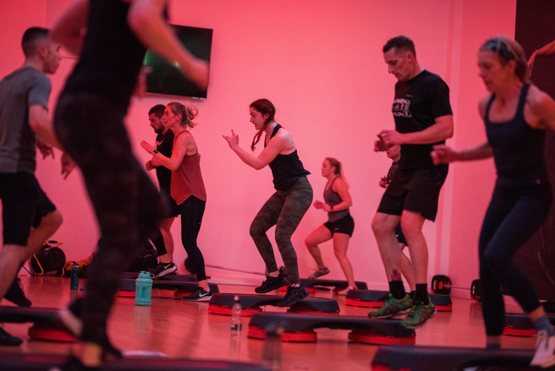 A group fitness class performs squats under pink lighting.