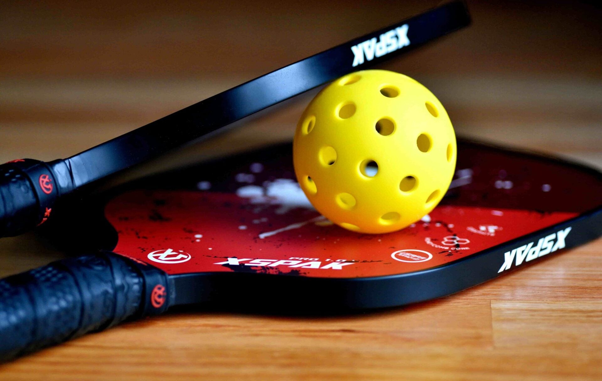 A close-up of a pickleball paddle and ball resting on a court.