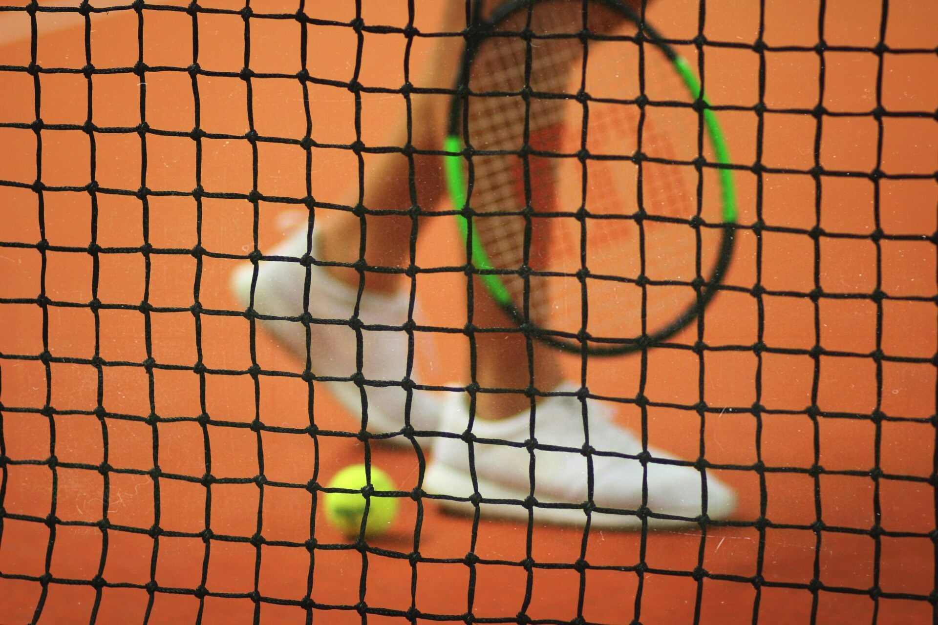 A close-up of a tennis racket and ball against a net.