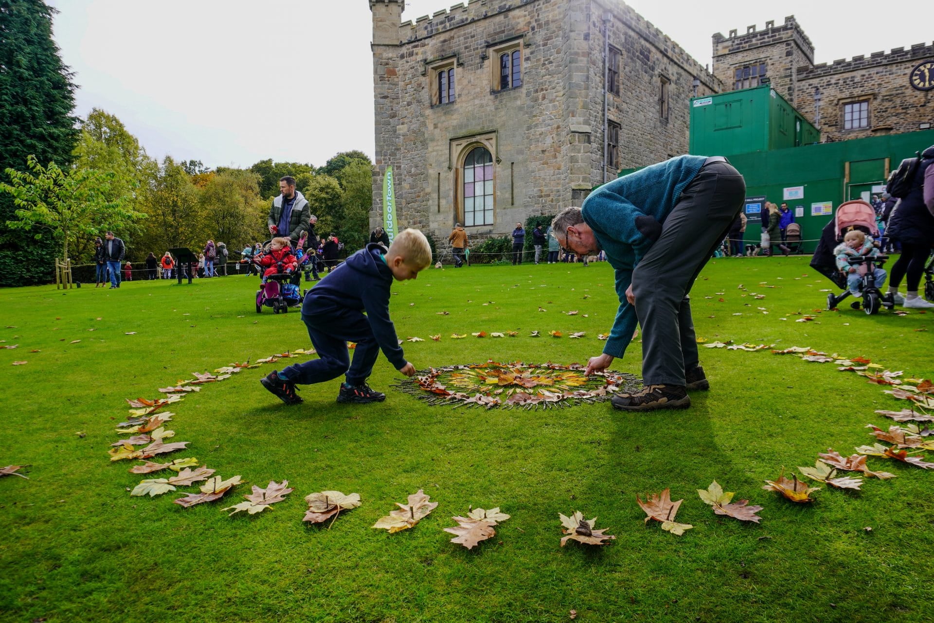 Two people plant or tend to flowers on a lawn outside a historic building.