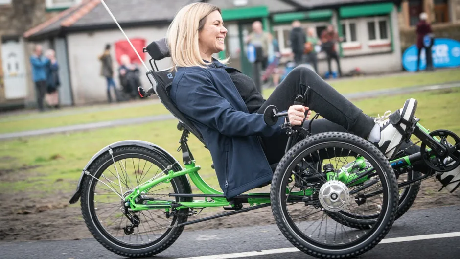 A smiling woman rides an adapted cycle outdoors.