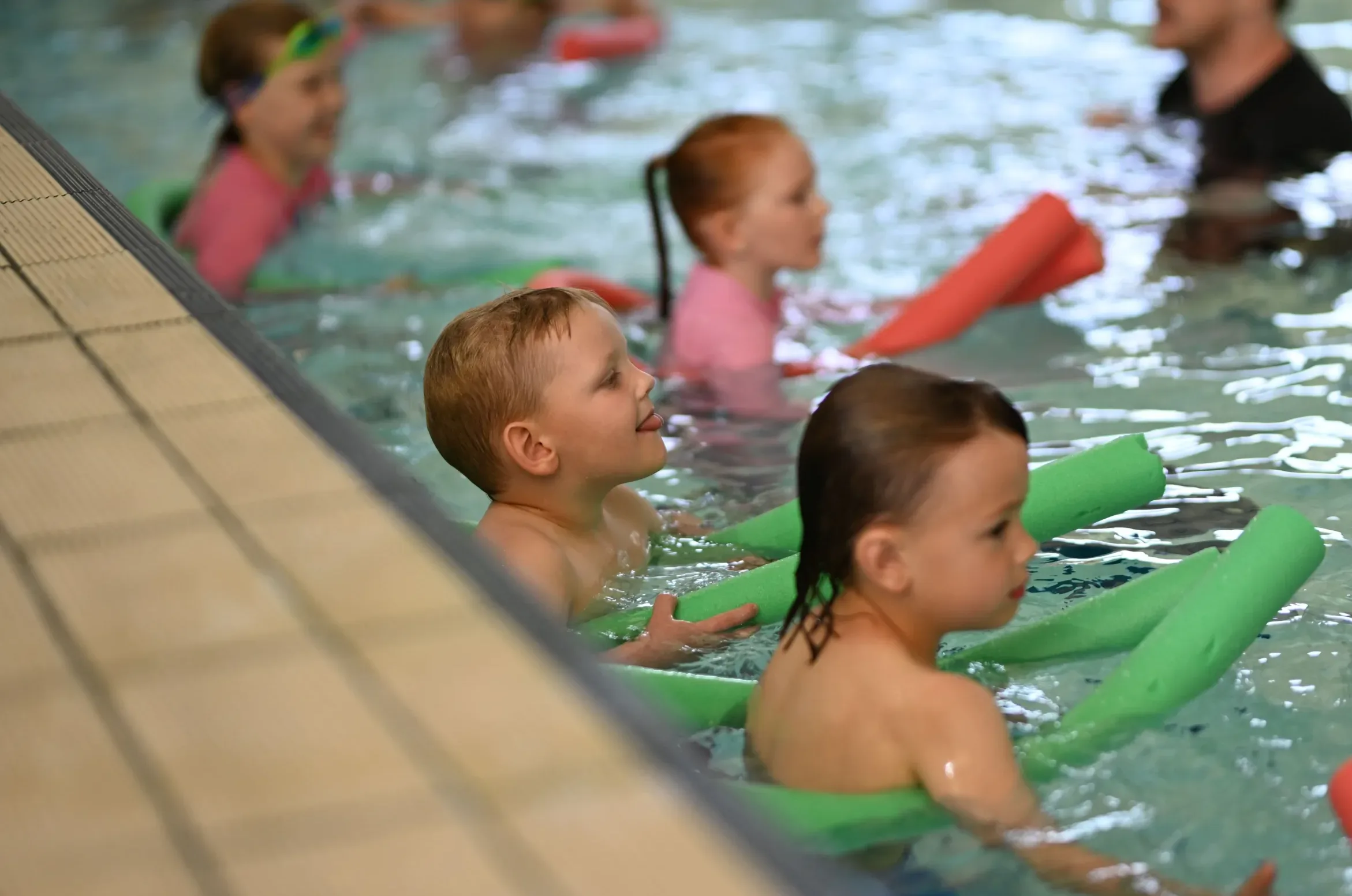 Children taking part in a swimming lesson using a pool noodle
