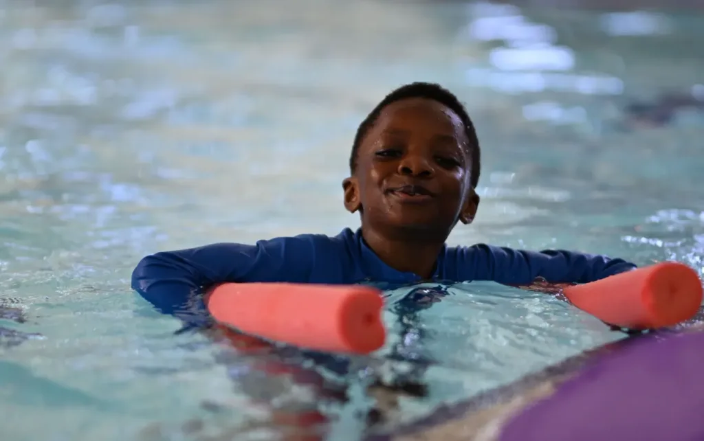 Young boy learning to swim with. pool noodle
